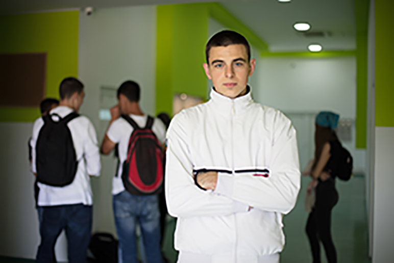 Portrait of male high school student. Students standing in school hallway.